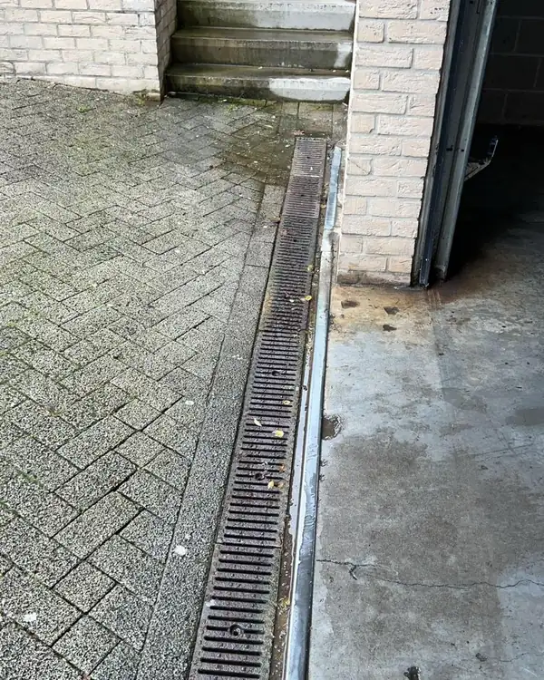 Caniveau à grille le long d'un bâtiment, avec dépôts et eau stagnante