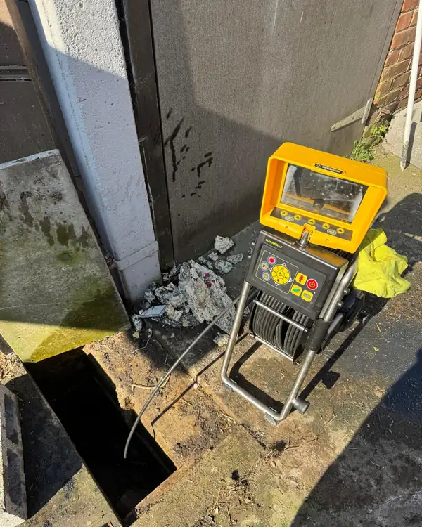 Caméra d'inspection jaune à côté d'une ouverture dans le sol donnant accès à une canalisation enterrée